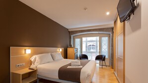 A modern hotel room with a large bed, bedside tables, a flat-screen TV, and a view of the outside.
