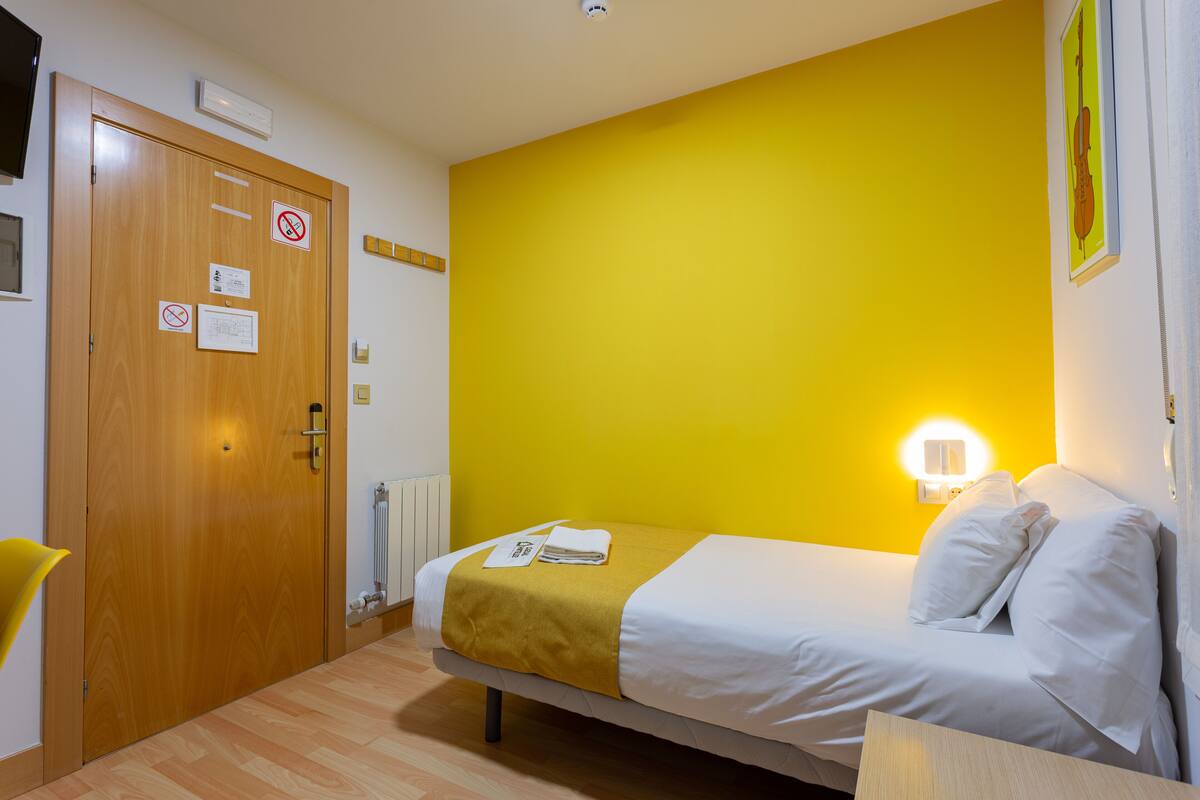 Una habitación con una cama, una puerta de madera, un radiador y una lámpara fijada a la pared.