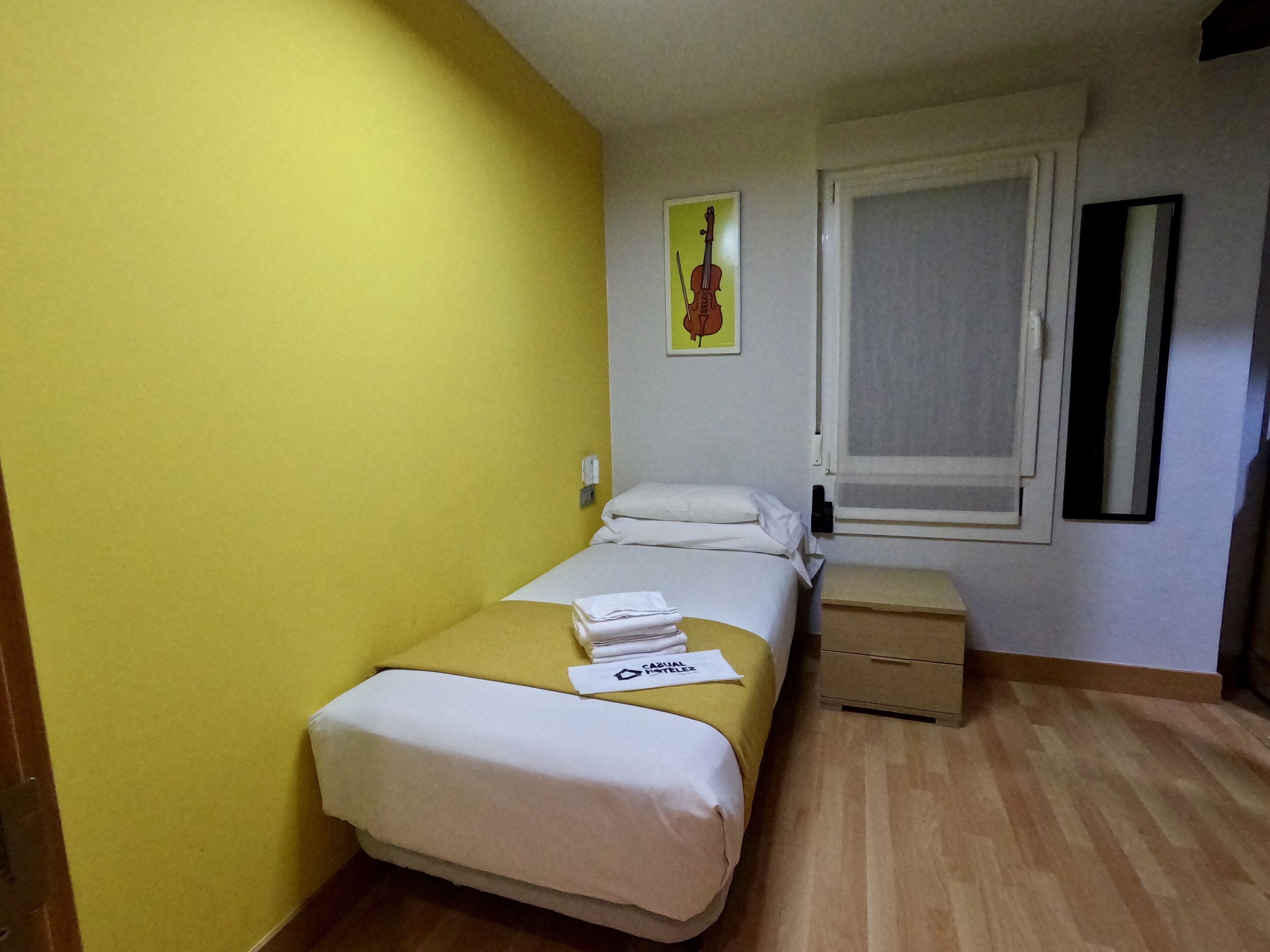 A small, neatly arranged bedroom with a bed, bedside table, and a window.