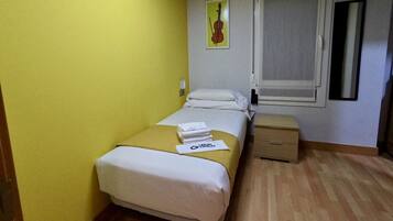 Un dormitorio pequeño y ordenado con cama, mesita de noche y ventana.