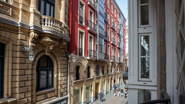A street view with historic buildings, a cobblestone street, and a staircase leading to an upper floor.