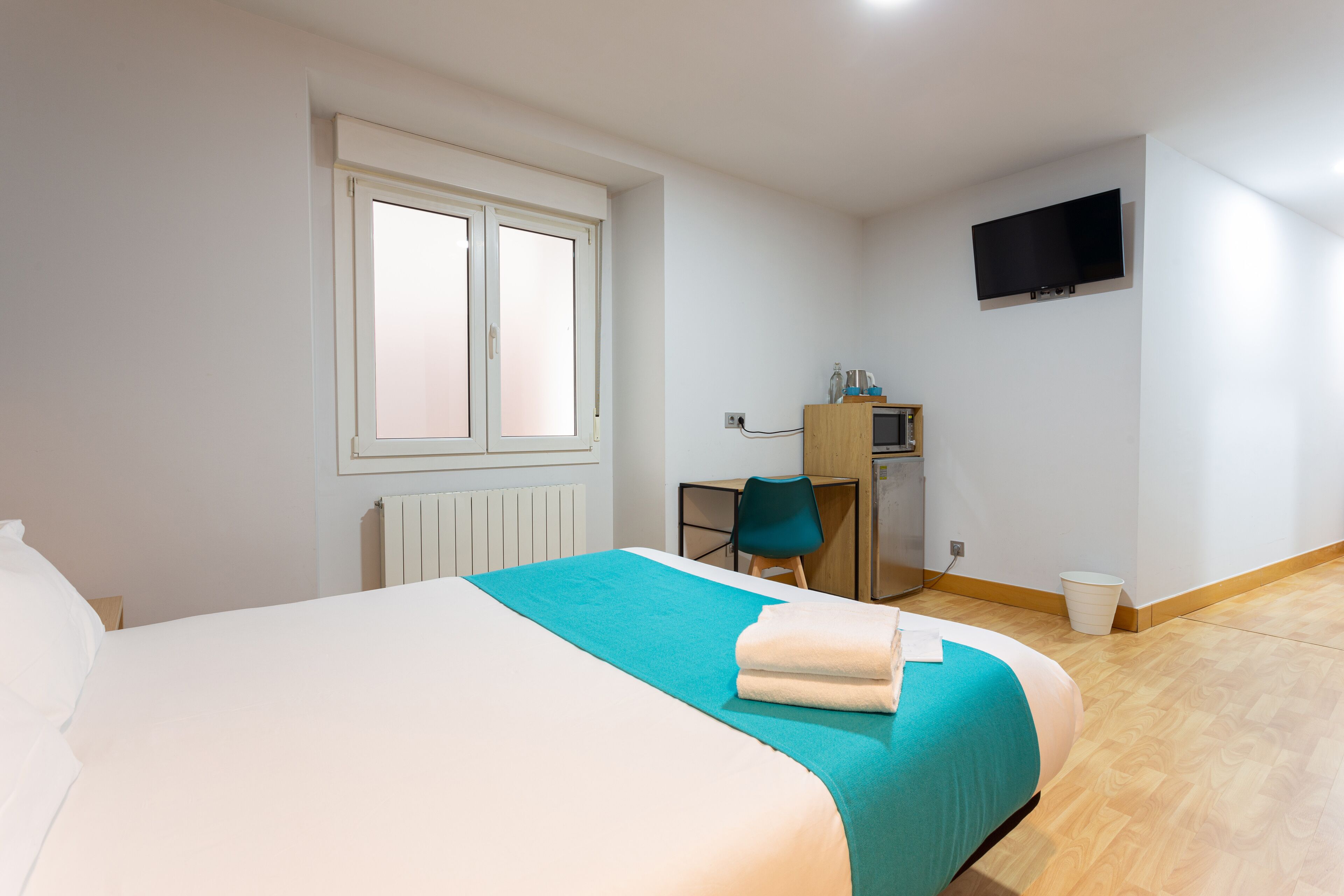 A hotel room with a bed, a desk, a chair, a television, and a window.