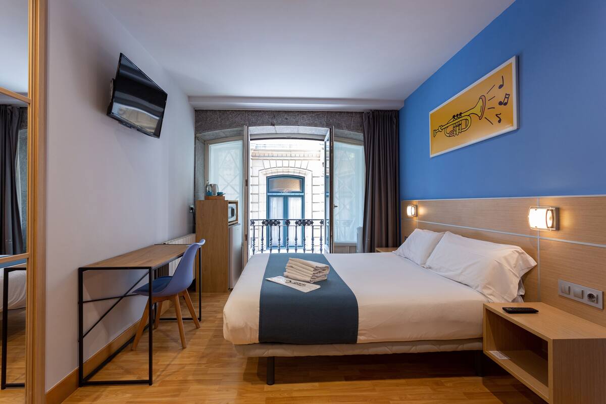 Una habitación de hotel con cama, escritorio, silla, televisión y un cuadro en la pared.
