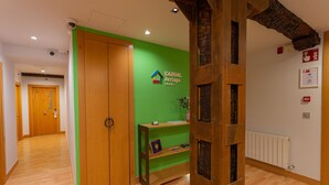 A hallway with wooden flooring, a green wall with a logo, a wooden door, and a shelf with a plaque.