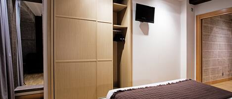A bedroom with a bed, a wardrobe, a television, and a newspaper on the wall.
