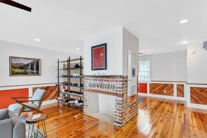 A modern living room with a brick fireplace, wooden flooring, a grey sofa, a wooden coffee table, and a bookshelf.