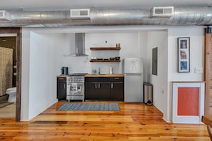 Cozinha compacta equipada com fogão, forno e frigorífico, piso de madeira e sistema de dutos visível no teto.