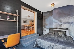 Quarto moderno com cama grande, escrivaninha com cadeira e vista para a área de jantar.
