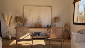 A cozy living room with a wooden coffee table, two wicker chairs, a white sofa, and a large abstract painting on the wall. - WOODEN HOUSE TYPICAL OF THE BASIN (Lège-Cap-Ferret)