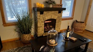 A cozy living room with a stone fireplace, a coffee table with a book, a glass of wine, and a basket.