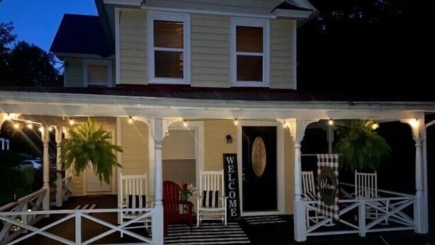 A two-story house with a porch, a welcome sign, and a black door.