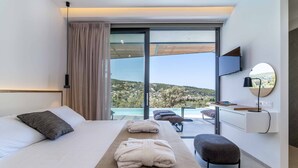 Una habitación de hotel moderna con una cama grande, una mesita de noche de madera, un banco y vistas a un paisaje montañoso a través de una puerta corrediza de vidrio.