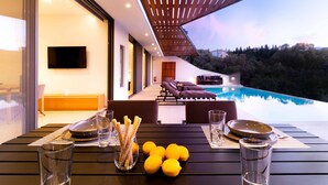 Un área de comedor exterior moderna con vista a la piscina, un televisor montado en la pared y una pérgola de madera.