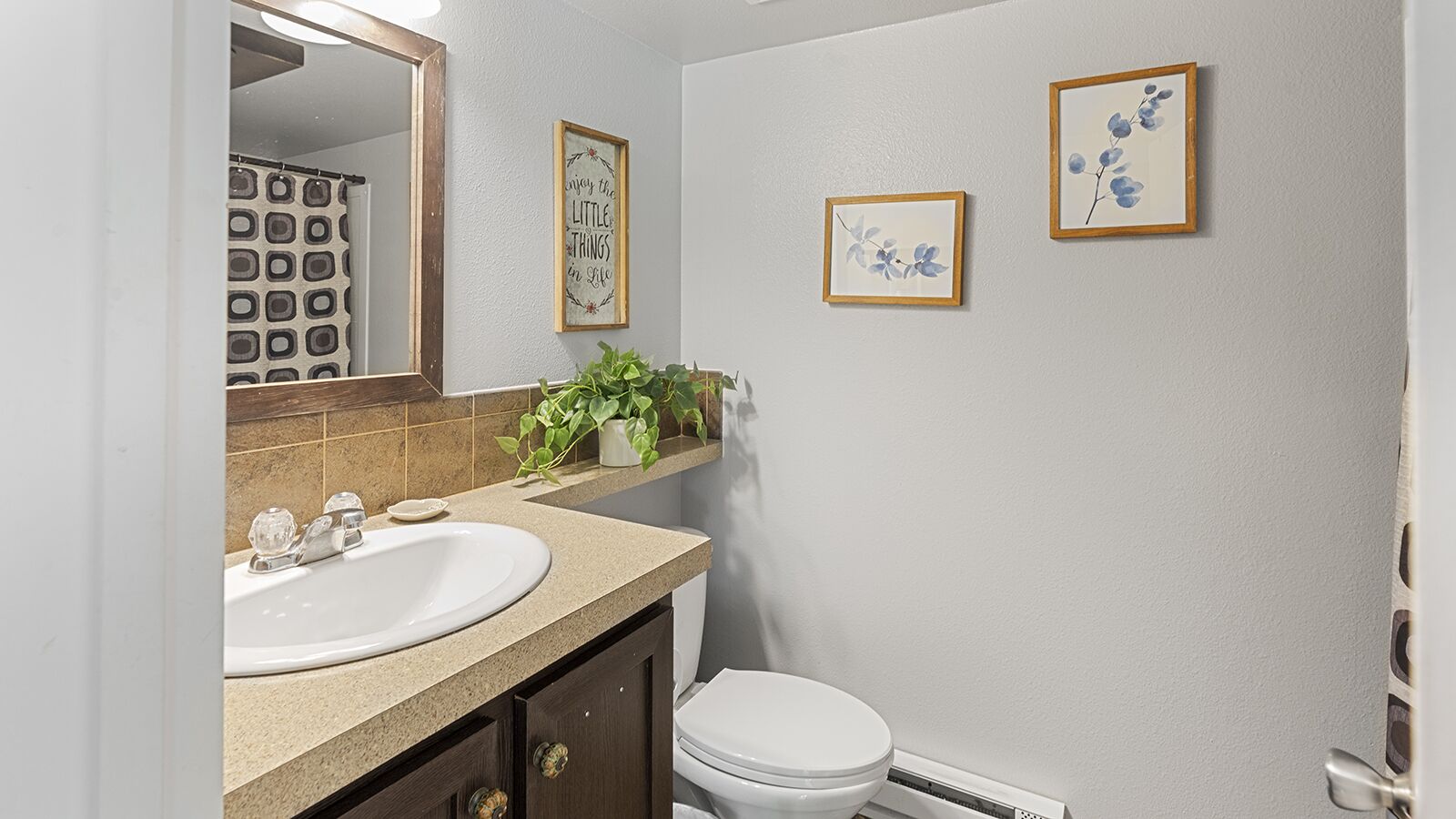 Un baño con un lavabo blanco, un espejo, un inodoro y dos cuadros en la pared.