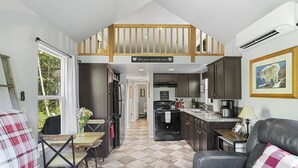 A cozy kitchen with dark cabinets, a wooden staircase, and a dining area with a checkered tablecloth. - Tiny Home@ Mt Rainier-Hot tub-AC (Ashford)