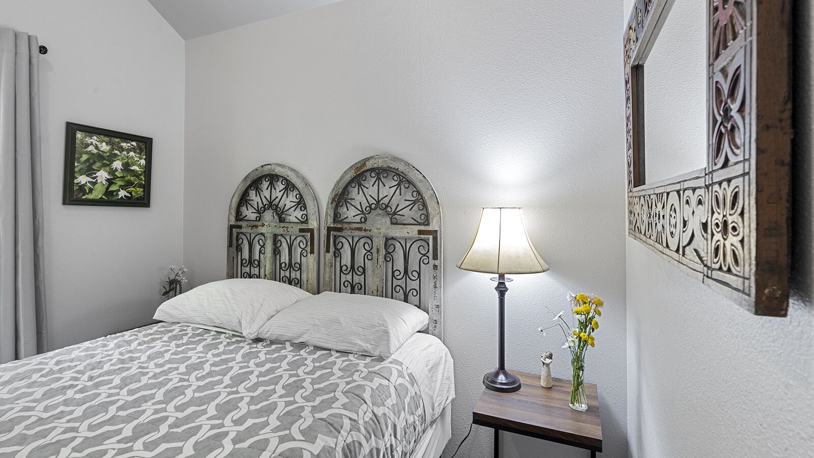 Un dormitorio con cama, mesita de noche con lámpara y espejo en la pared.