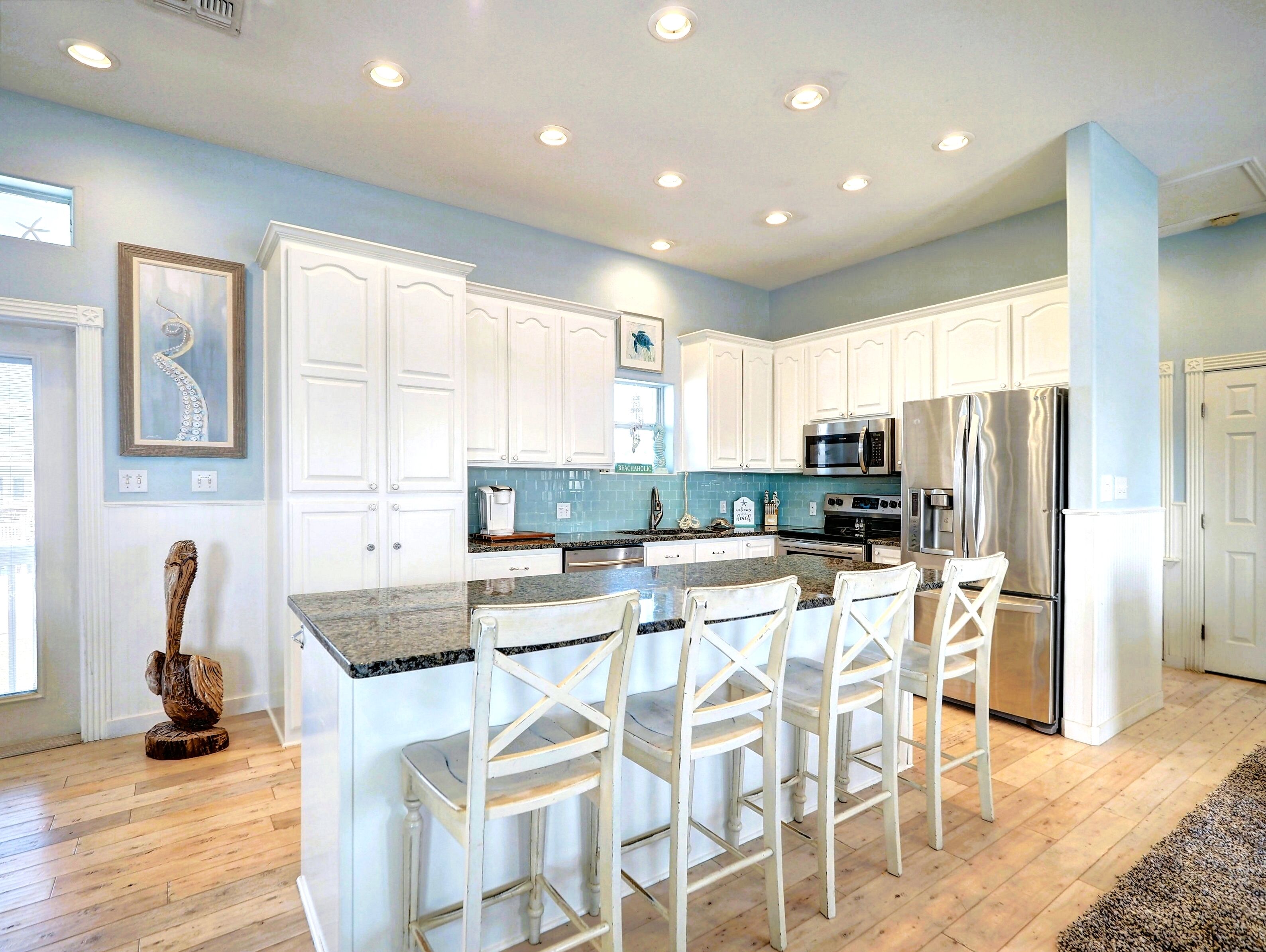 A modern kitchen with white cabinets, a granite countertop, stainless steel appliances, and a bar area with white chairs.
