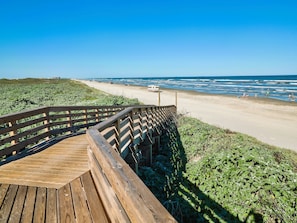 A wooden boardwalk leading to a beach with a vehicle parked on the sand.
