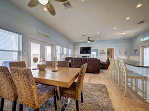 A spacious living room with a wooden dining table, brown leather sofas, and a TV mounted on the wall.