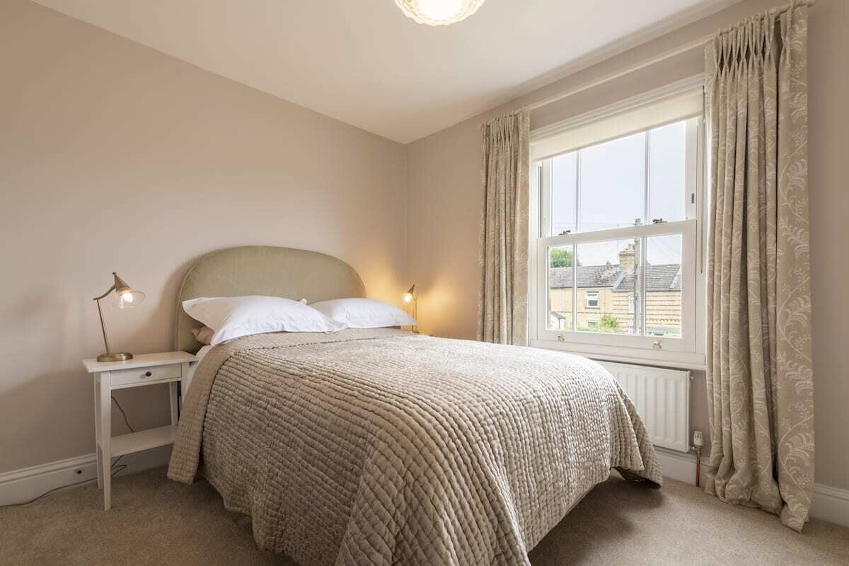A bedroom with a bed, nightstand, lamp, and window with curtains.