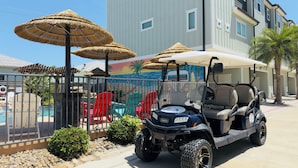 Un carrito de golf estacionado cerca de una piscina con sombrillas y sillas.
