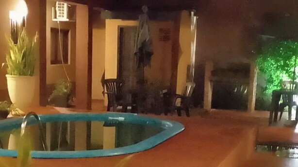 A pool area with a blue pool, potted plants, and outdoor furniture. - Residencial Los Pinos (Puerto Iguazú)