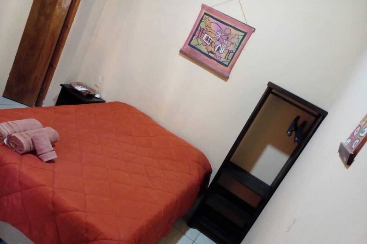 A bedroom with a bed, a nightstand, a mirror, and a wall-mounted picture.