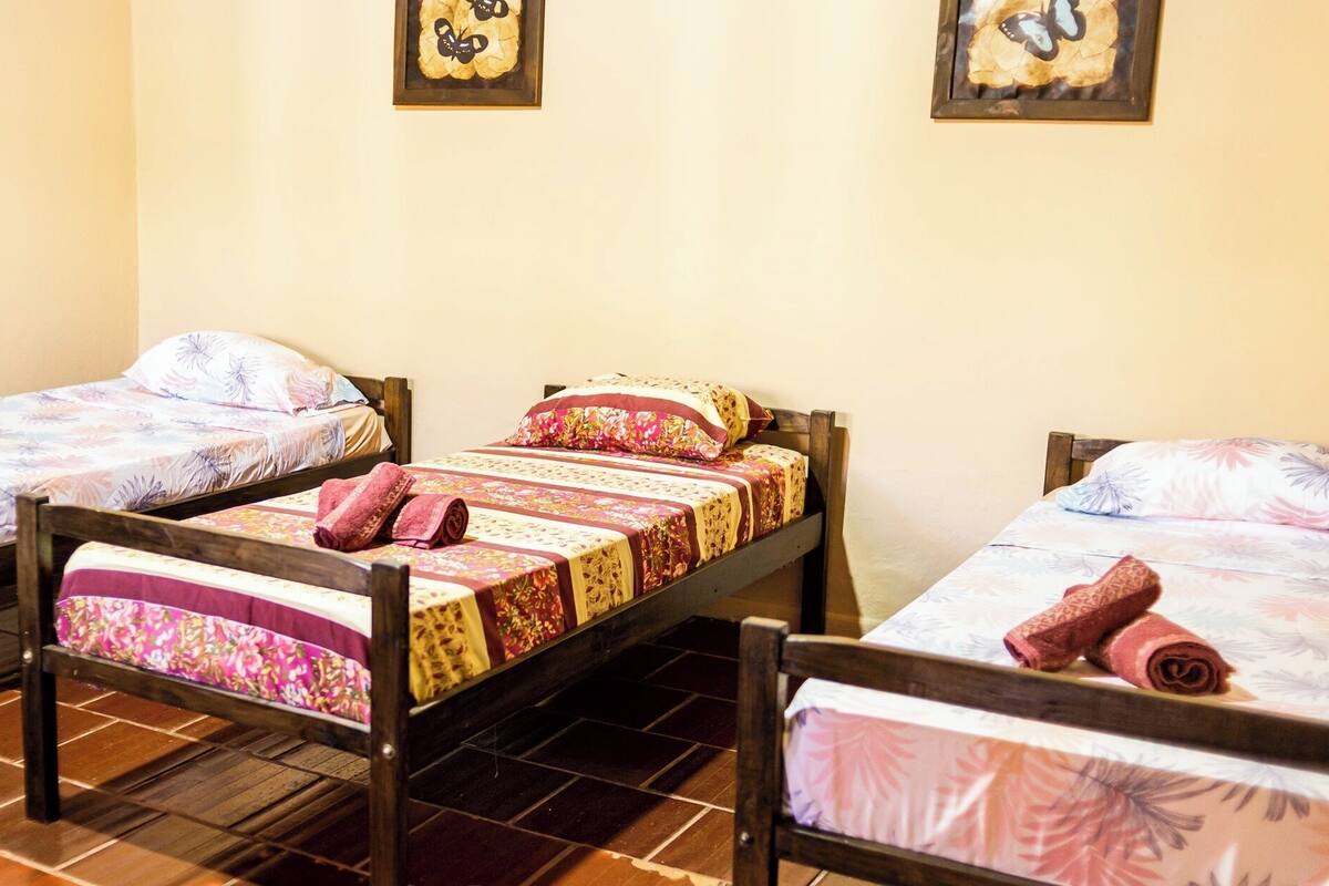 A hotel room with three wooden beds, each with floral bedding and rolled towels.