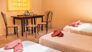 A hotel room with two beds, a dining table with chairs, and a window with curtains. - Residencial Los Pinos (Puerto Iguazú)