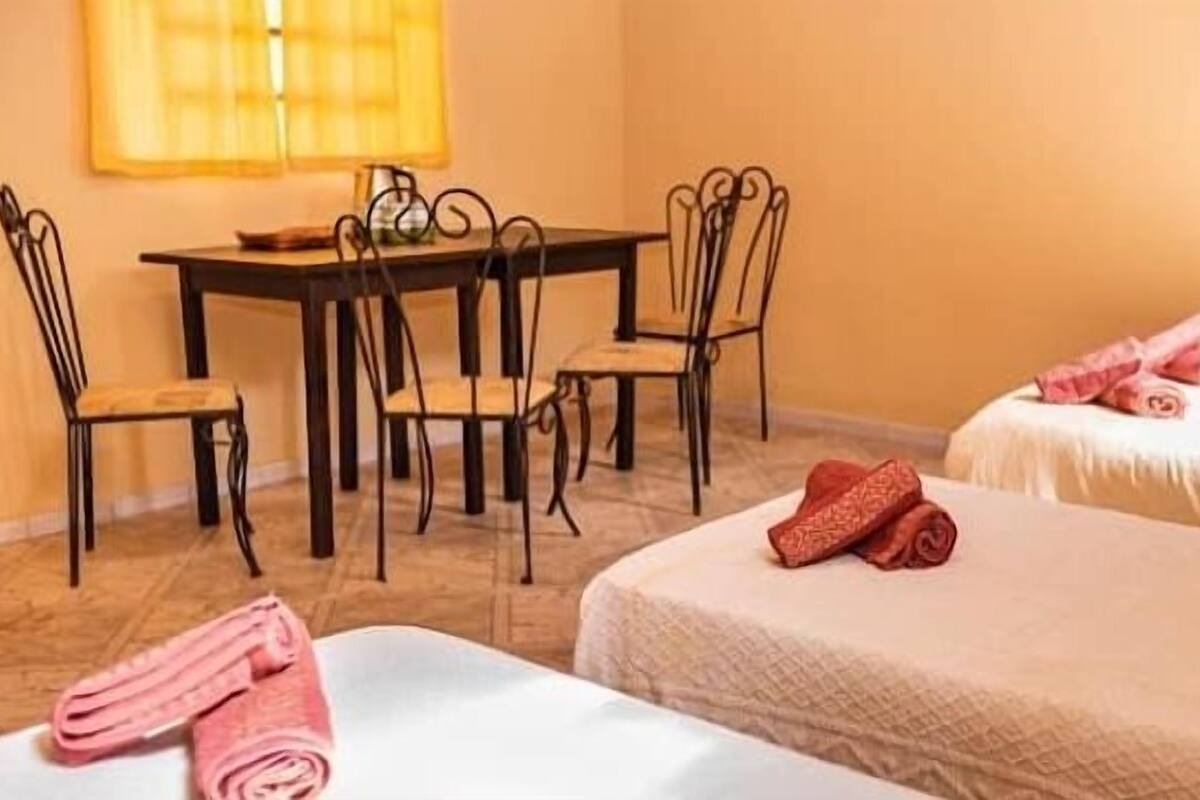 A hotel room with two beds, a dining table with chairs, and a window with curtains.