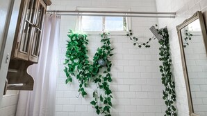 A bathroom with white tiled walls, a white ceiling with decorative panels, a chandelier, and green plants hanging on the wall. - The Chandelier House of Midtown - Near It All! (Memphis)