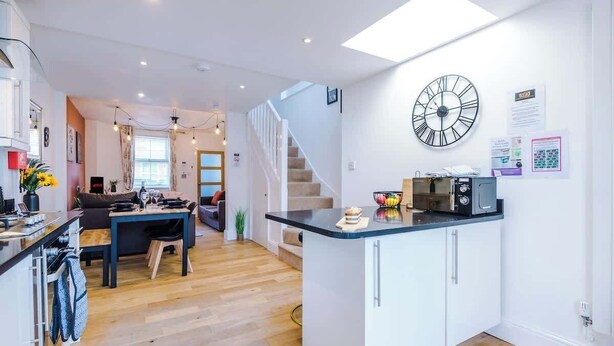 Een moderne keuken met een centraal eiland, een zithoek met een bank en tafel, en een trap naar een ander niveau.