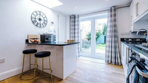 Een moderne keuken met een centraal eiland, barkrukken, een klok en uitzicht door grote schuifdeuren.