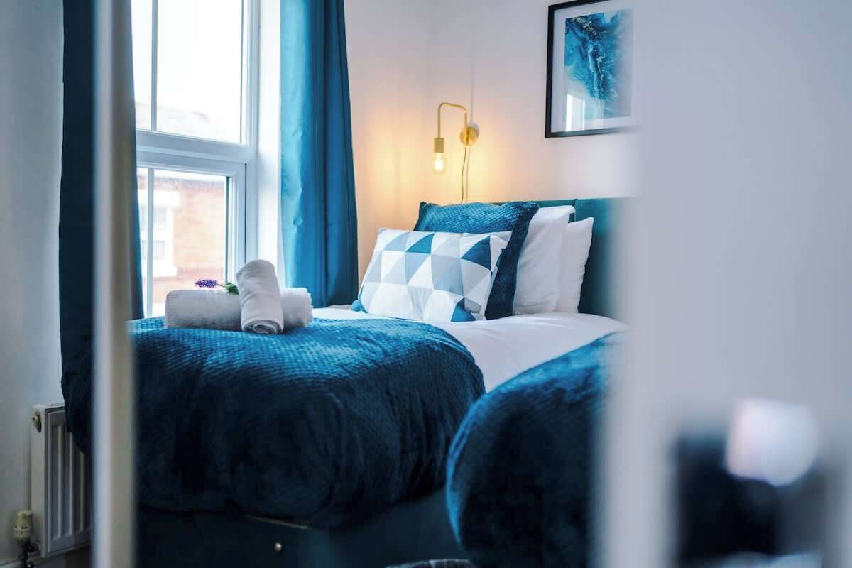 Un dormitorio con cama, mesita de noche, lámpara y ventana.