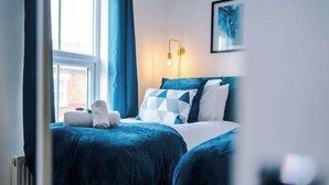 Een slaapkamer met een bed, nachtkastje, lamp en raam.