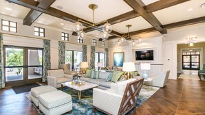 A spacious living room with a large sofa, ottomans, and a coffee table. There are multiple windows and a television mounted on the wall. - “Magical Memories Manor” - Awesome Movie and Game Rooms (Kissimmee)