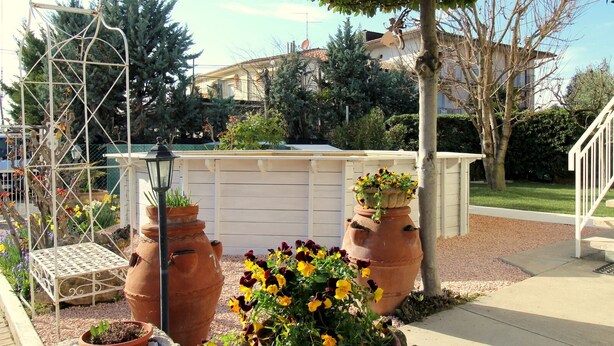 Ein Garten mit Terrakottatöpfen, einem Metall-Rankgerüst und einem weißen Zaun.