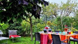 Ein Essbereich im Freien mit einem Tisch für vier Personen, umgeben von Stühlen und einem Grill in der Mitte.