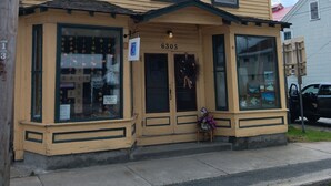 A two-story building with a yellow facade, numbered 6305, featuring large windows, a front entrance, and a small display window with pictures. - Trailside Townhouse in the center of Indian Lake (Indian Lake)