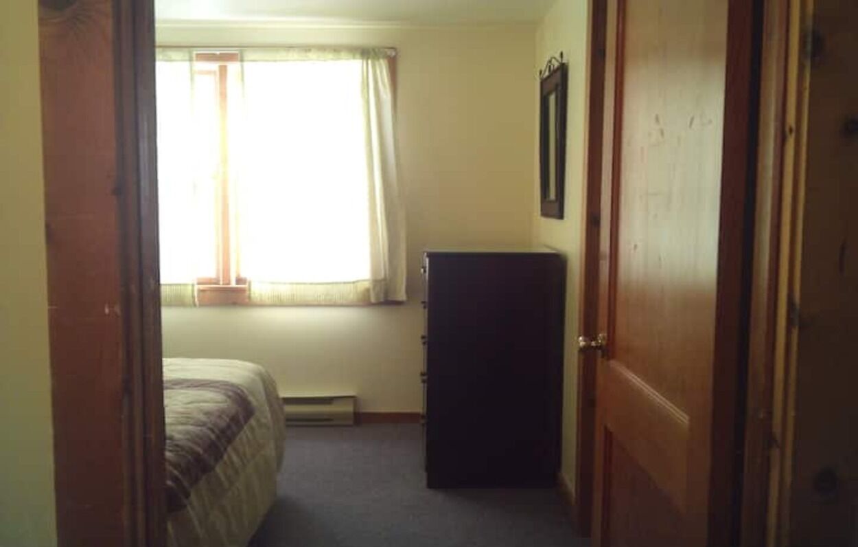 A bedroom with a bed, a window with curtains, a radiator, and a door.