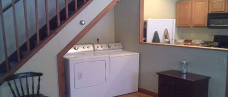 A laundry room with a washer and dryer, wooden cabinets, a small table, and a chair.