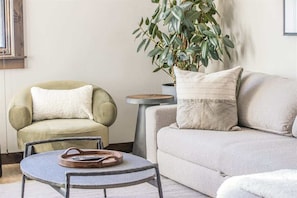 Una sala de estar con un sillón verde, un sofá color beige, una mesa redonda y una planta en maceta.
