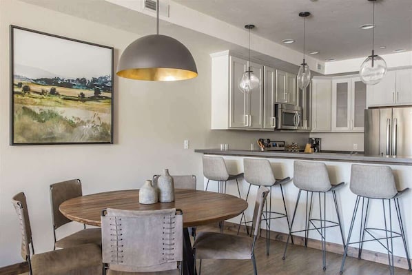 Een moderne keuken met een centraal eiland, hanglampen en een eethoek met stoelen en een tafel.