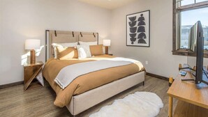 A bedroom with a bed, bedside tables, a desk, a television, and a large window. - Middle Of Town Center, Luxury Two Bedroom Condo (Big Sky)