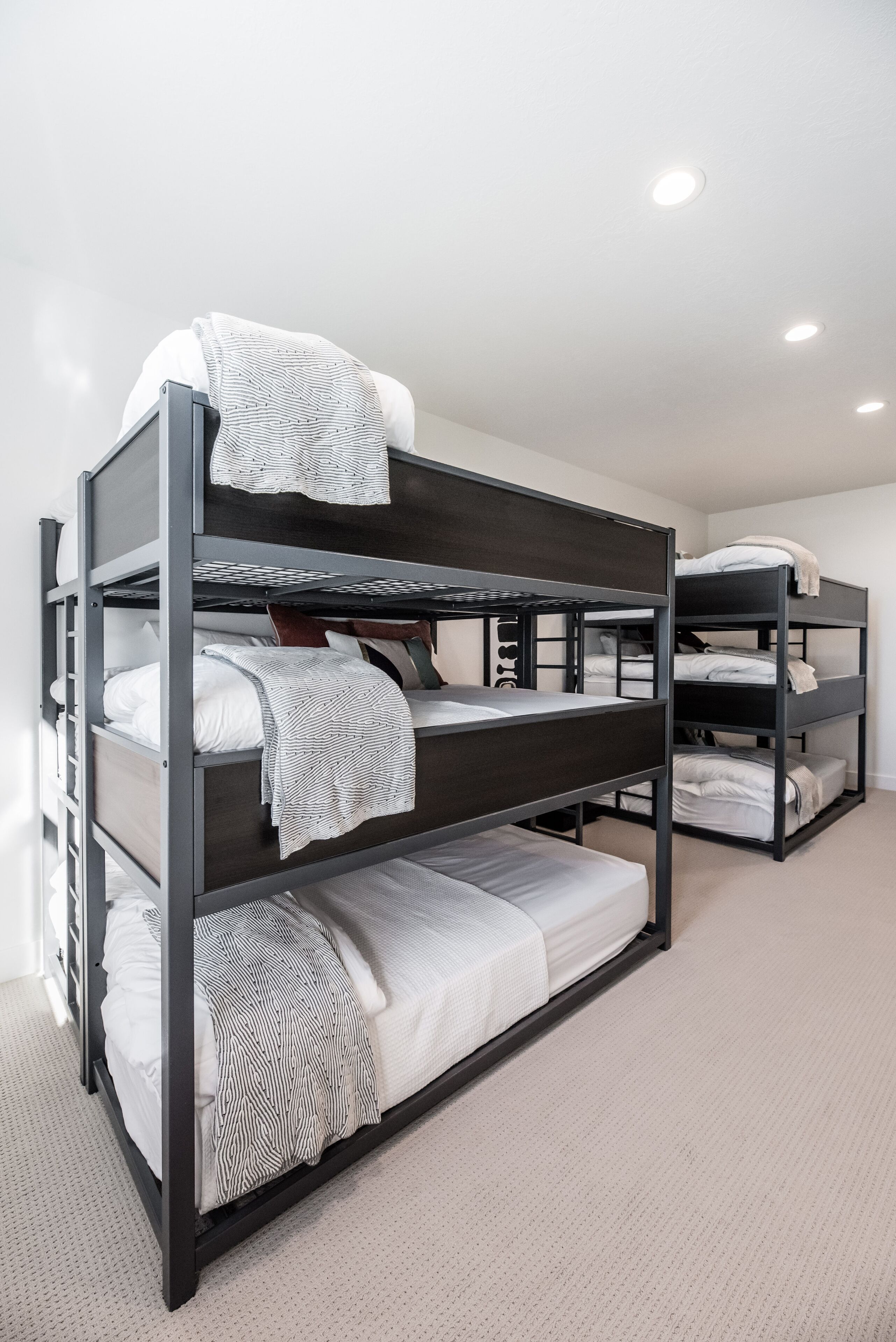 A bunk bed room with three levels, white bedding, and a light-colored carpet.