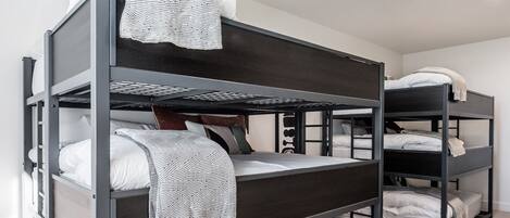 A bunk bed room with three levels, white bedding, and a light-colored carpet.