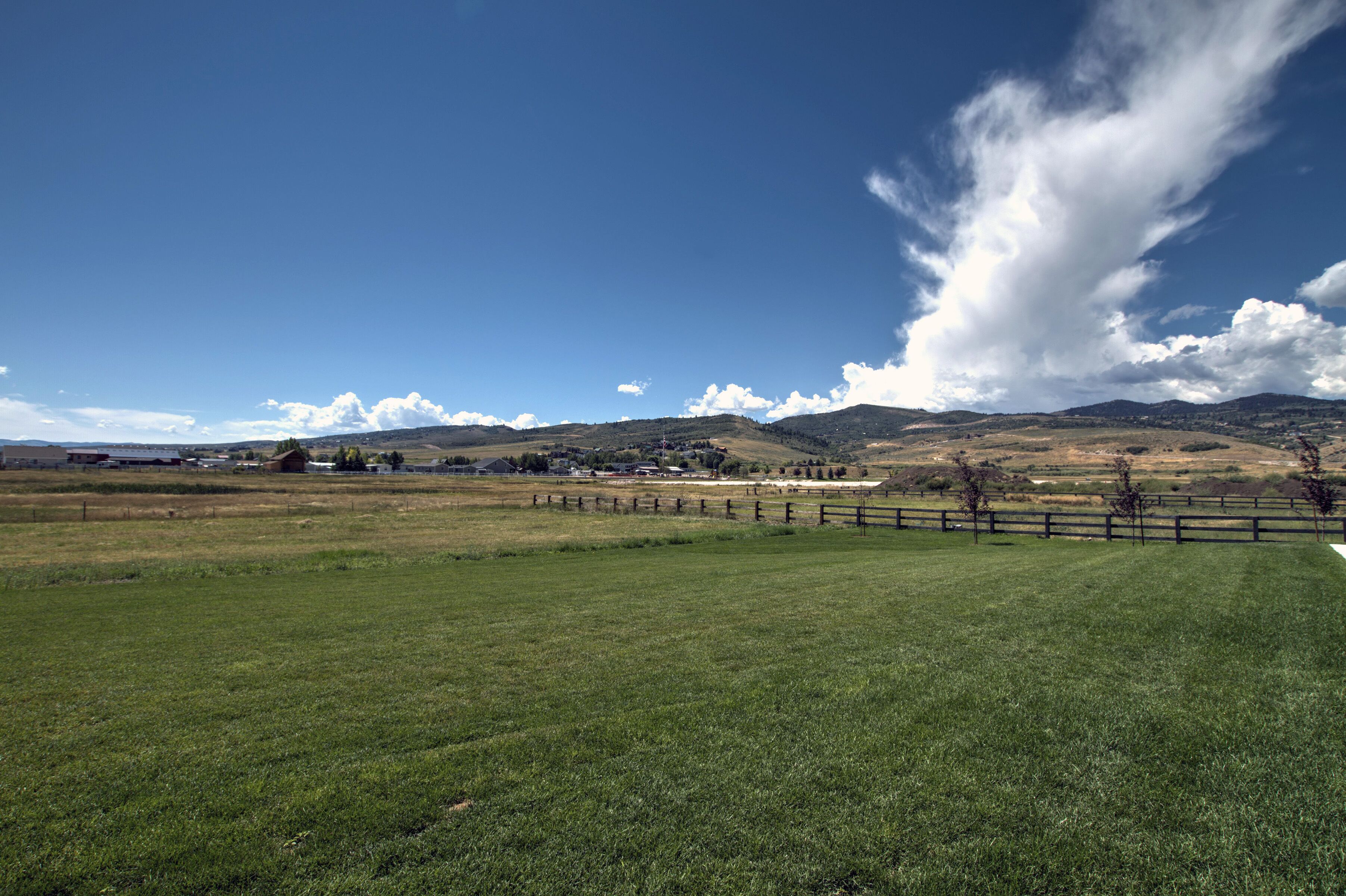 A grassy field with a wooden fence, a clear sky, and distant hills.