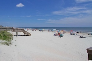 Una playa con un muelle de madera, sombrillas y gente disfrutando.