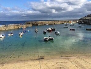 A harbor with various boats anchored in clear water, a stone breakwater, and a rocky coastline. - The Loft House - a beautiful 3 storey cottage (Mousehole)