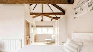 A bedroom with a large bed, a wooden ceiling, a radiator, and a window.